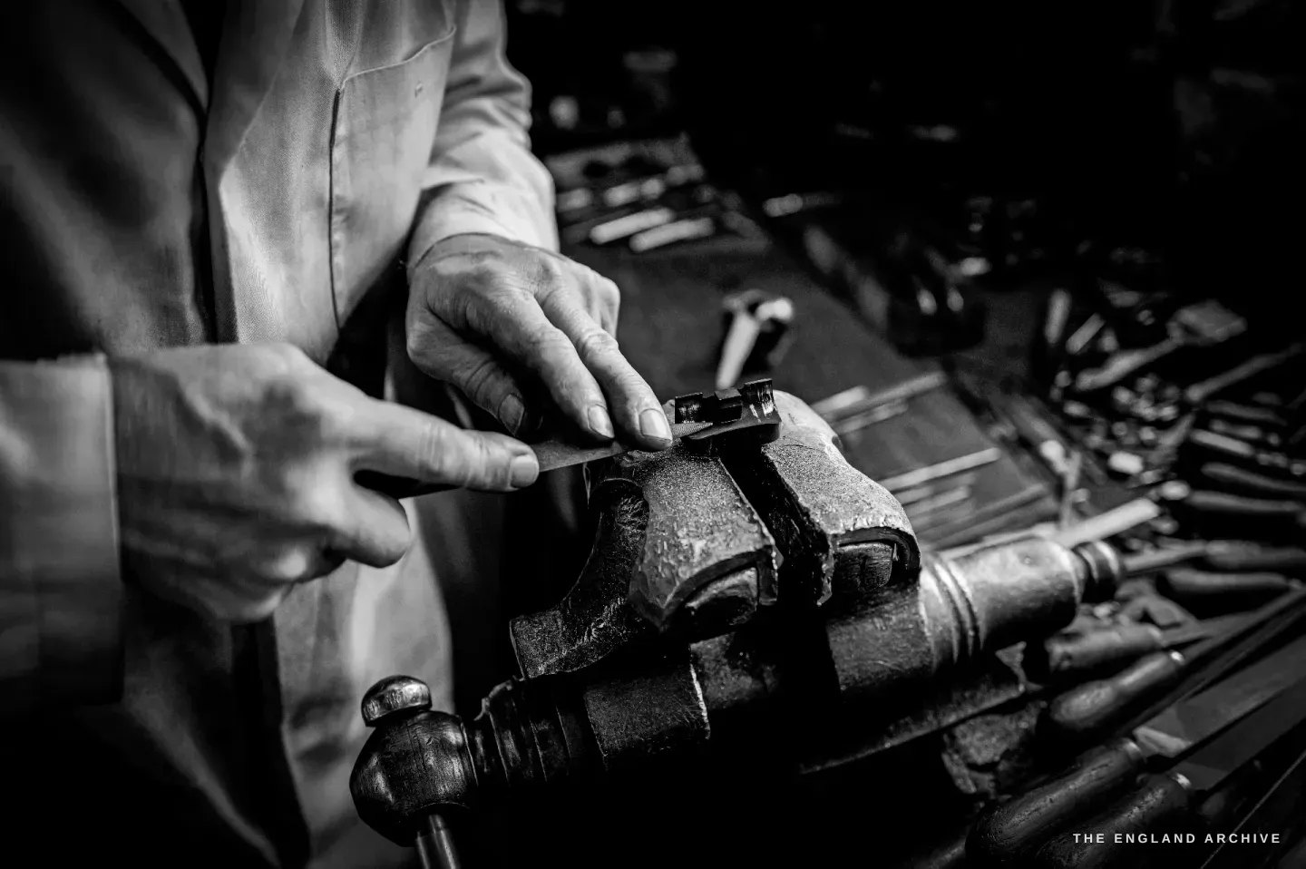 Haydn Hill files a small part held in the bench vice, a rack of files laid out along the bench beside his hands.