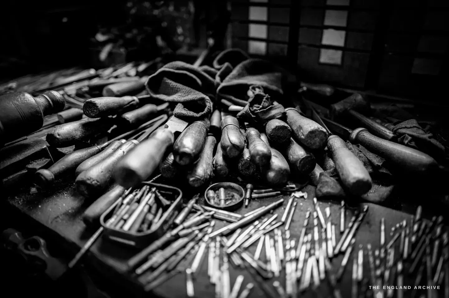 A bench crowded with dozens of worn file handles and hand tools laid out together, their steel and wood catching the light.