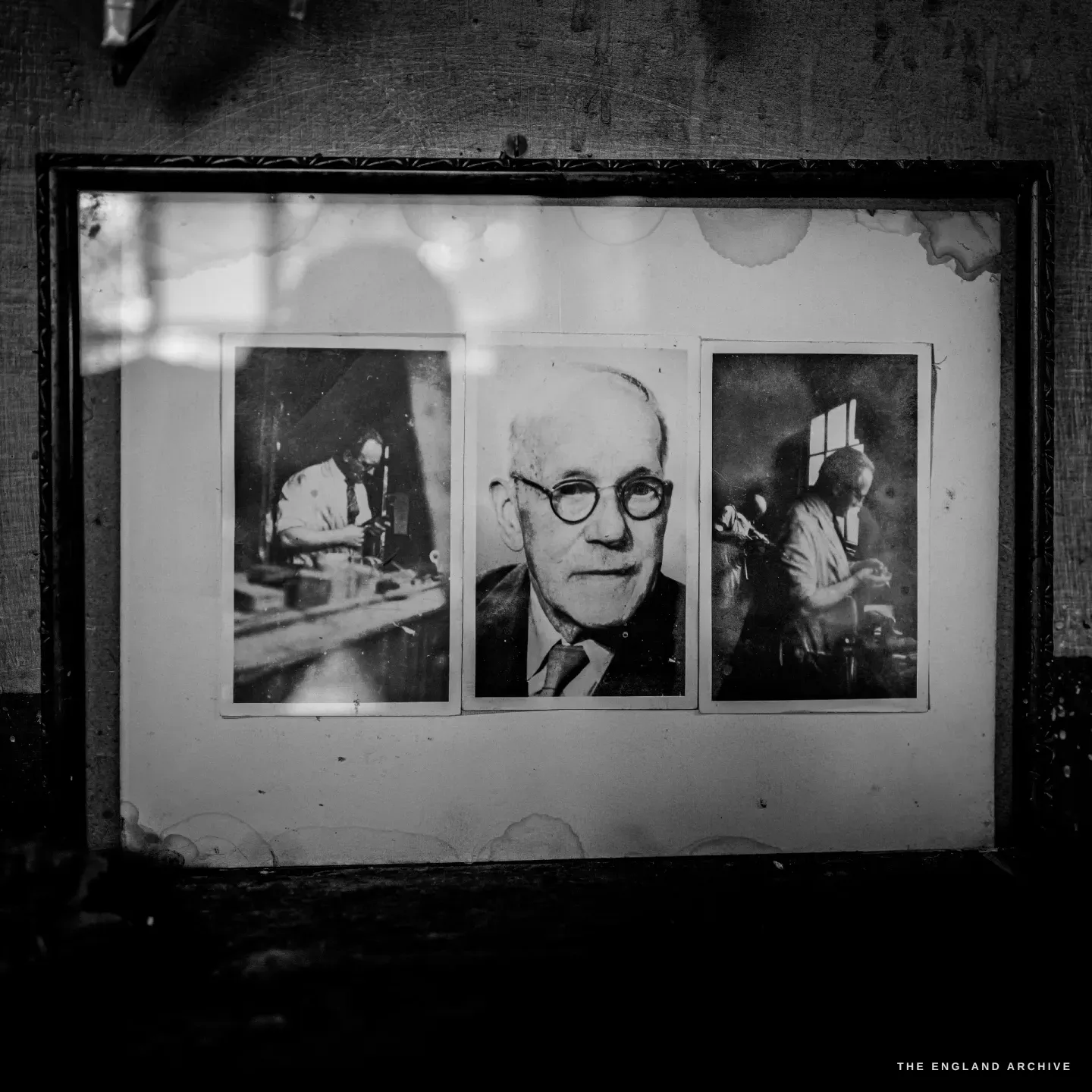 A framed set of old photographs on the workshop wall: a bespectacled gunmaker in a collar and tie at the centre, flanked by two working views of him at his bench.
