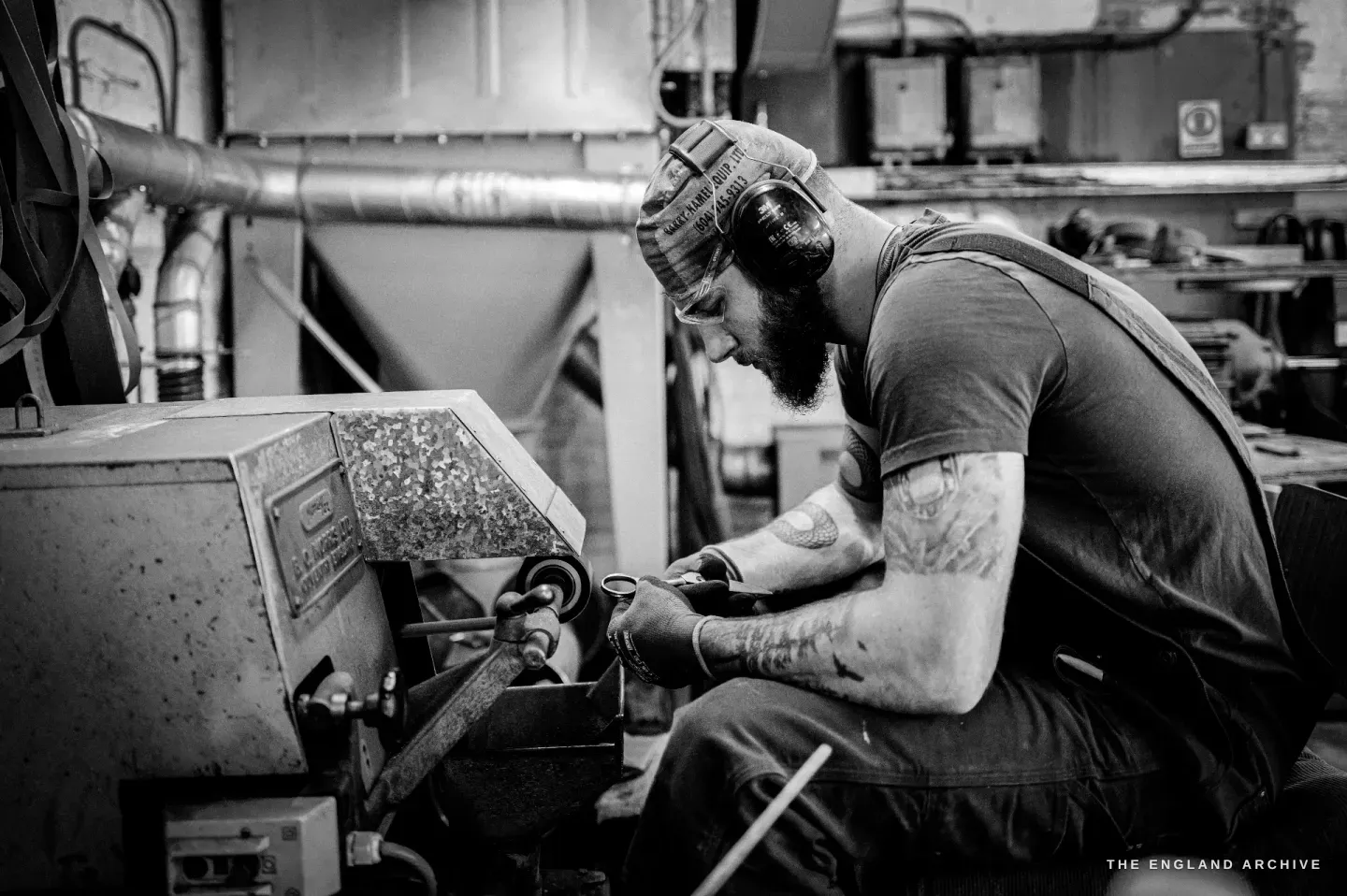 James seated side-on at the grinding machine, working a blade, the extraction hood and bench behind him.