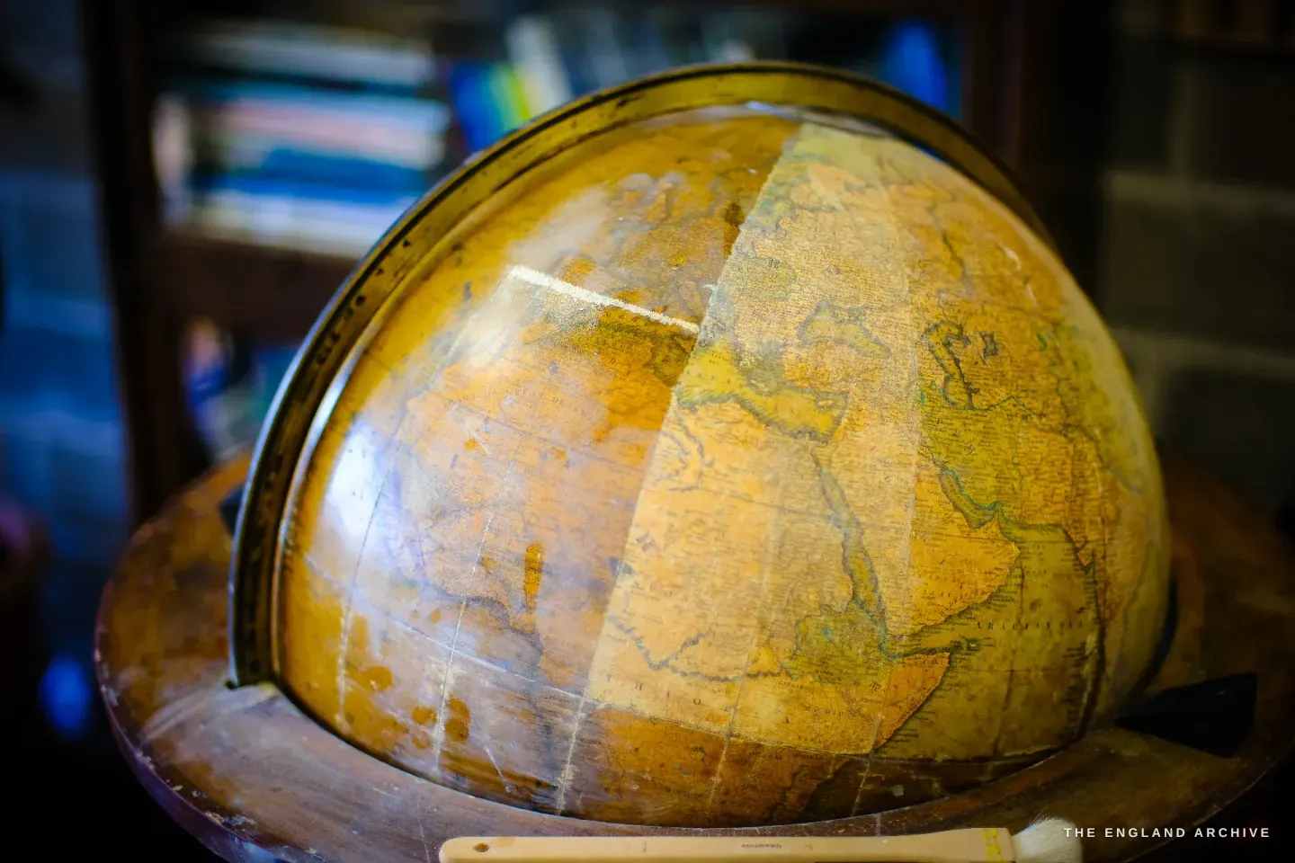 An antique terrestrial globe part-way through restoration, one cleaned segment bright against the darkened aged surface, set in a brass meridian and wooden horizon ring.