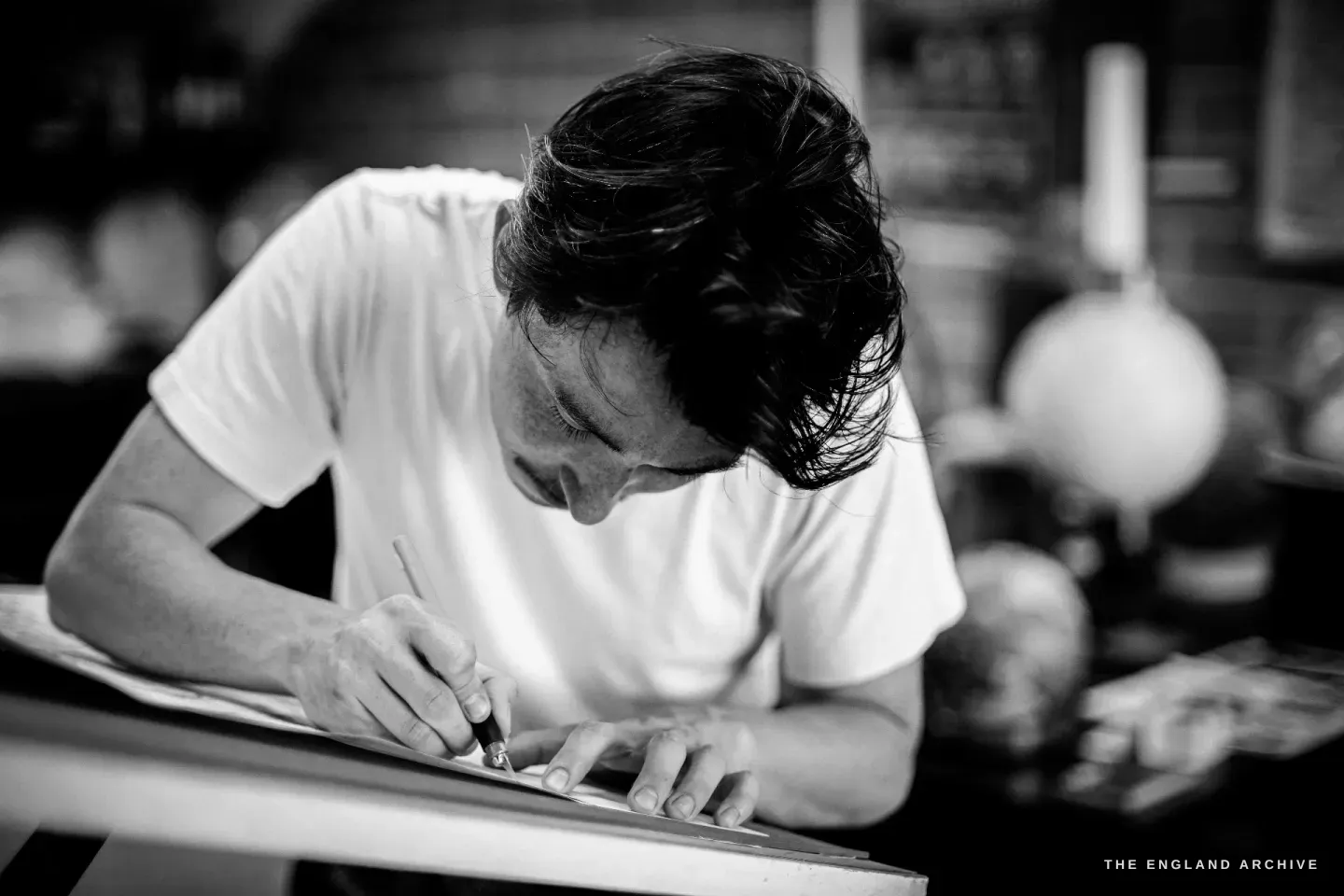 Jonathan bent close over the bench, scoring a printed map sheet with a fine blade.
