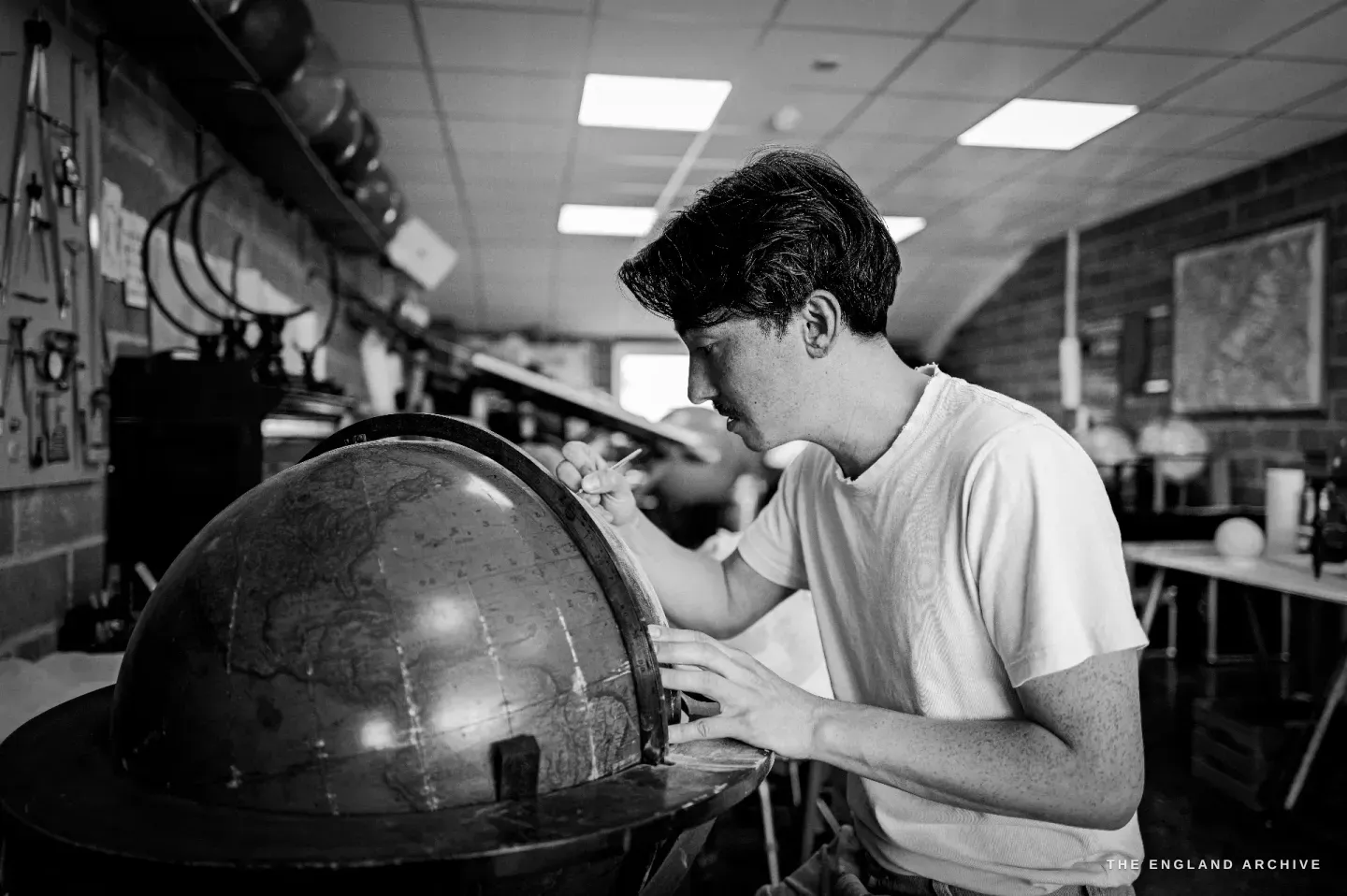 Jonathan in profile working on a large aged globe, the workshop tool wall and a framed map behind him.