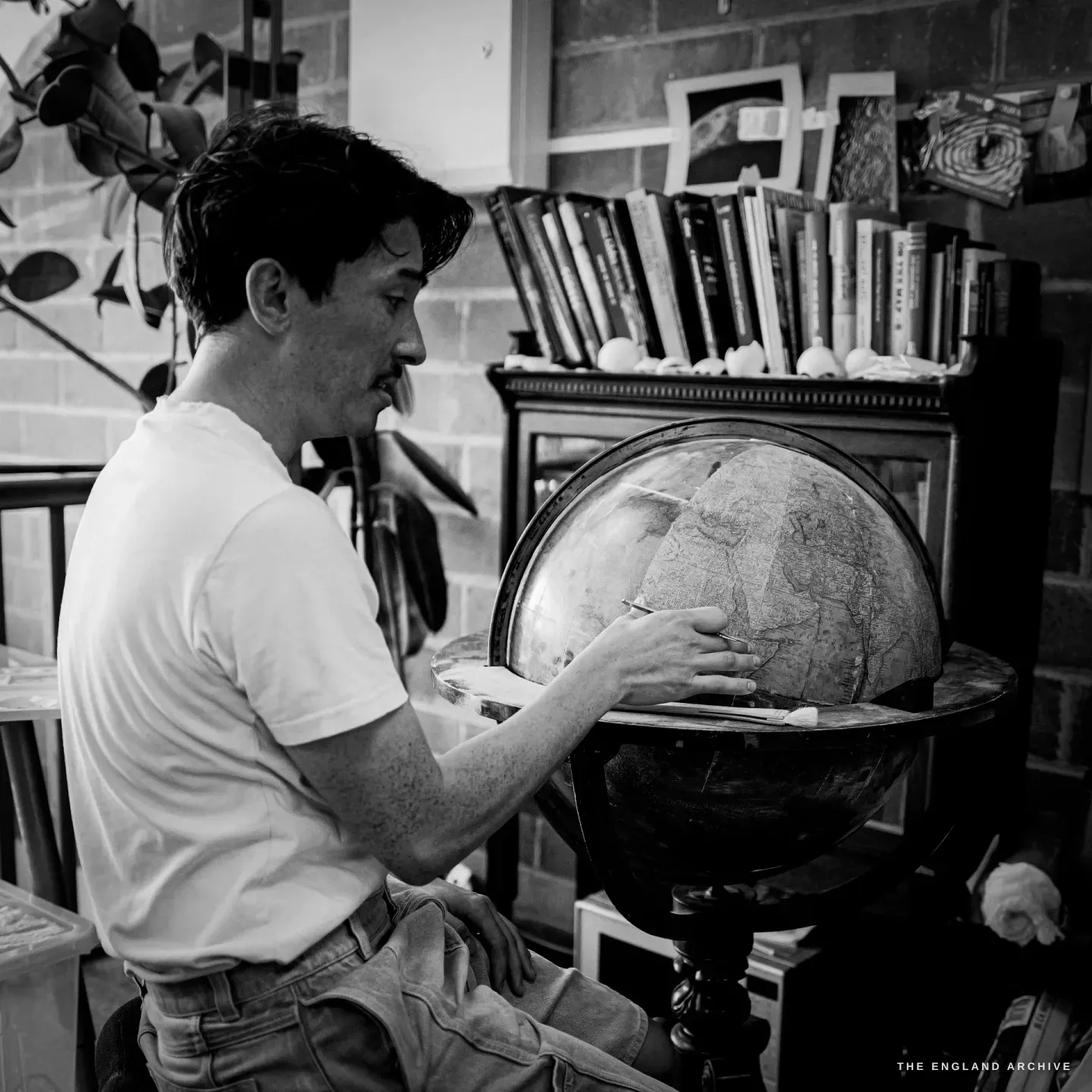 Jonathan seated, working the surface of an antique globe on a turned stand, a bookshelf of reference behind him.