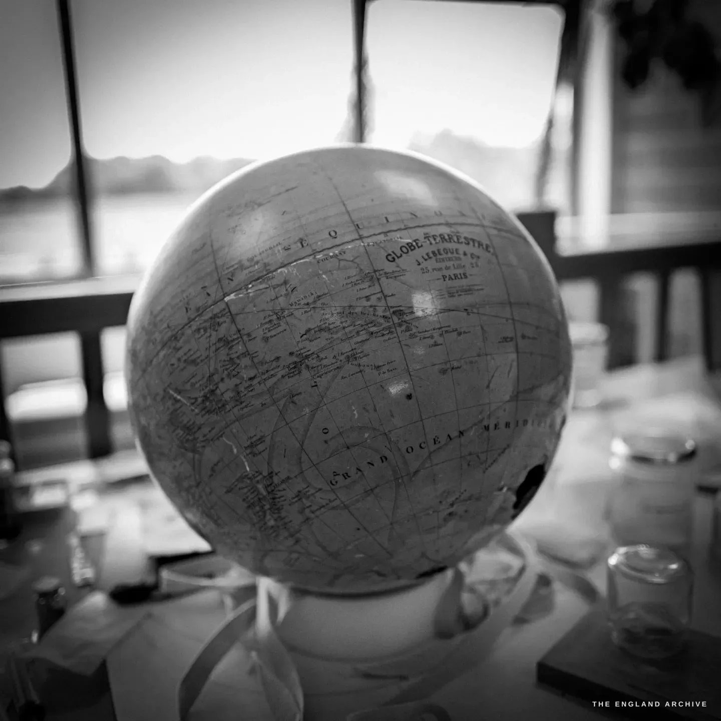 A close view of an antique French terrestrial globe, its cartouche reading Globe Terrestre, Paris, the window and countryside soft behind.