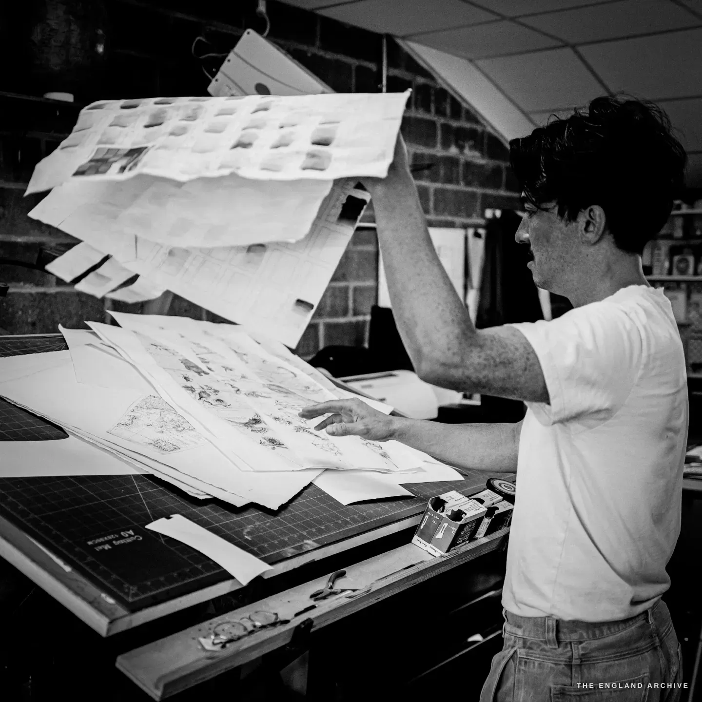 Jonathan at a cutting mat lifting large printed sheets of map gores, a craft knife on the bench.