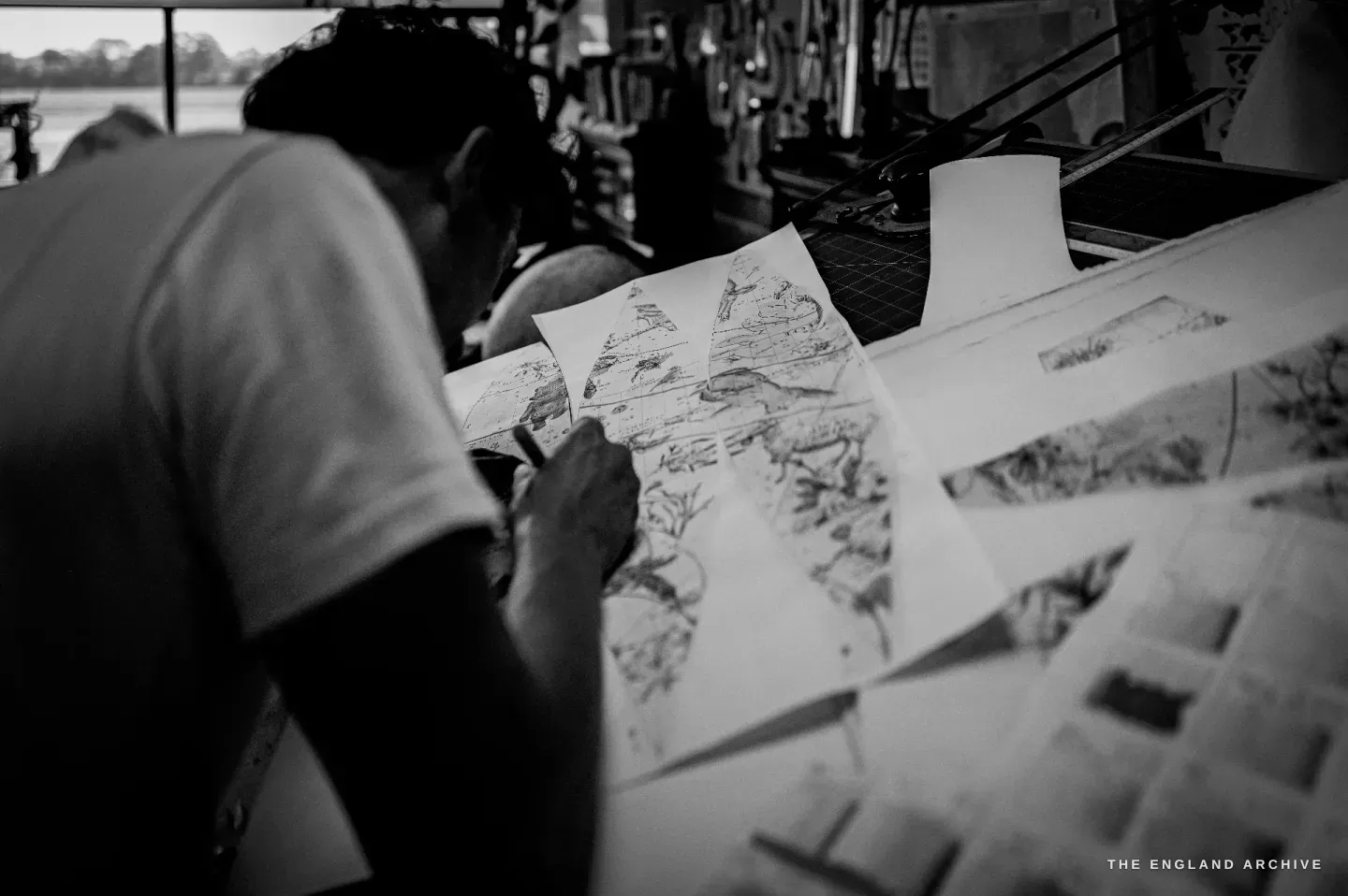 Over Jonathan&rsquo;s shoulder, a printed map gore showing fine terrain and a decorative sea creature, his hand working the sheet.