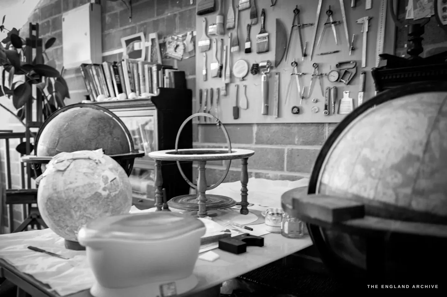 Three stages on one bench: a raw plaster globe core, an empty stand with its meridian ring, and a finished antique globe.