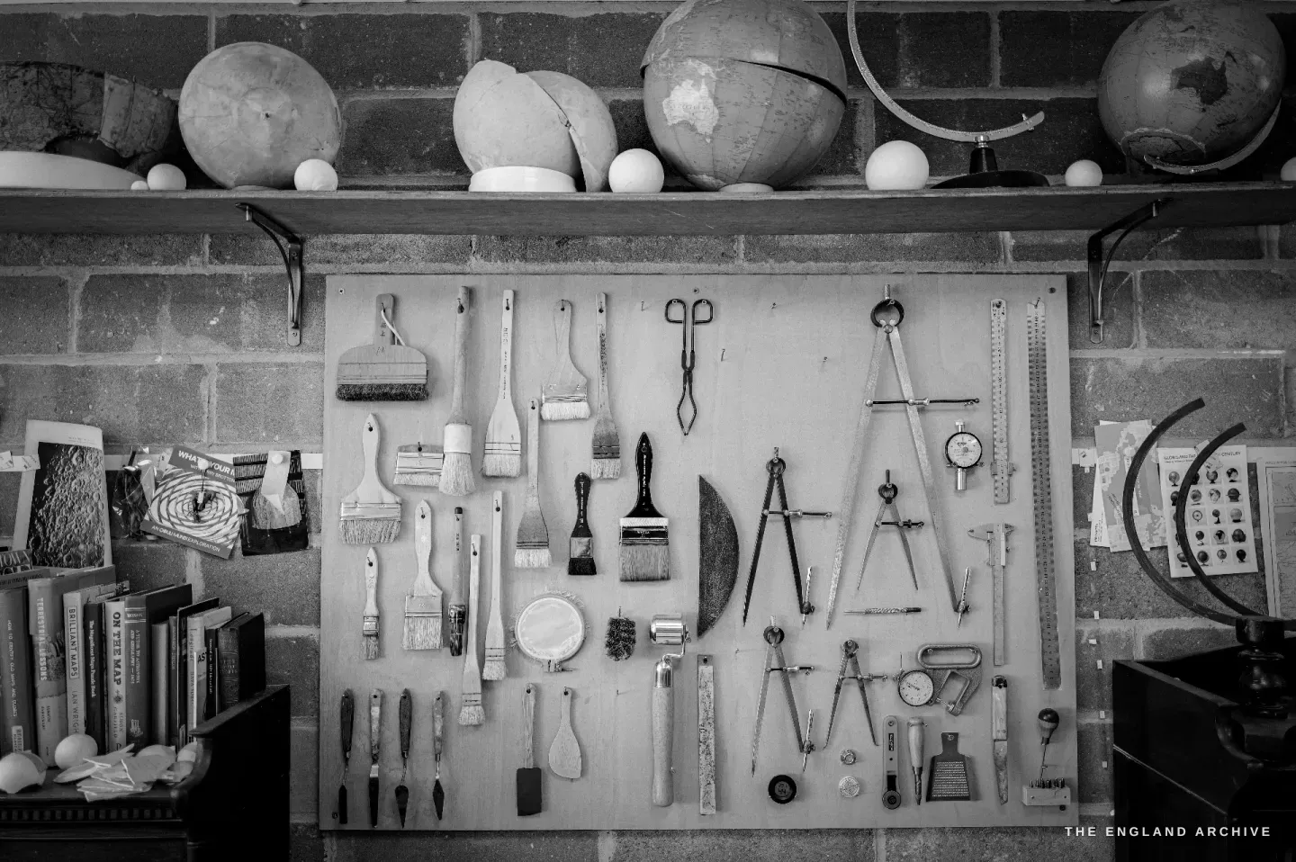 A pegboard wall of globemaking tools - brushes, dividers, calipers, rulers, scissors - with globe cores on the shelf above.