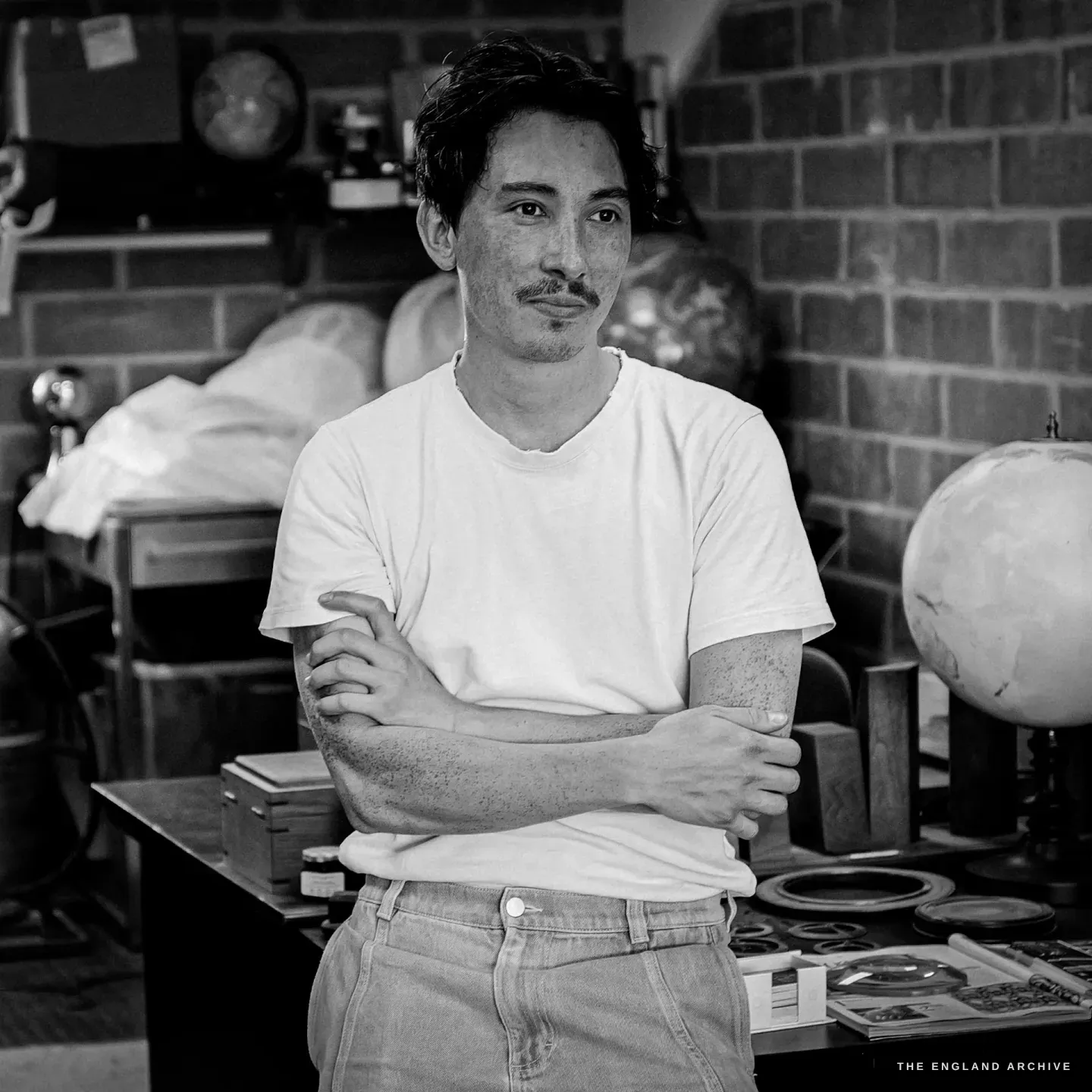 Jonathan Wright with his arms folded, looking directly at camera, globes and tools behind him.