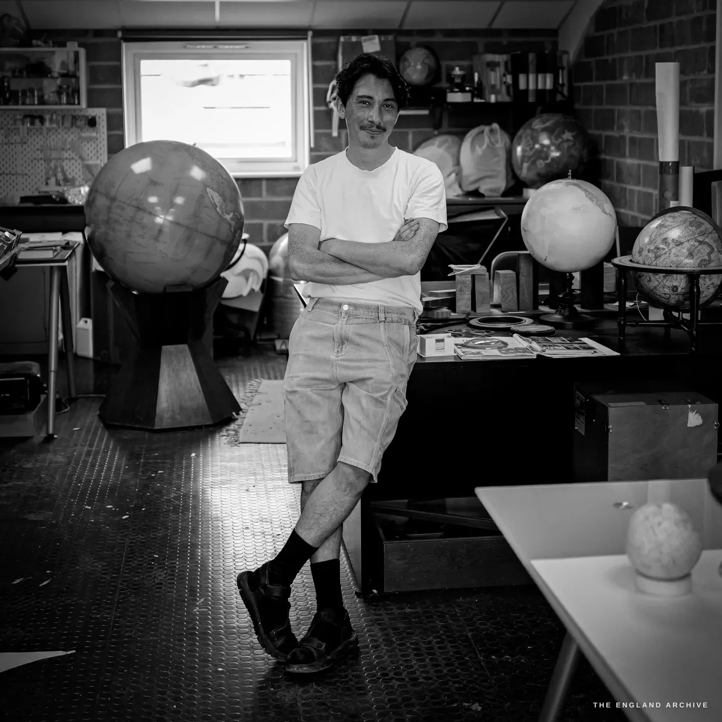 Jonathan leaning against a bench with his arms folded and ankles crossed, a large globe on a wooden stand beside him.