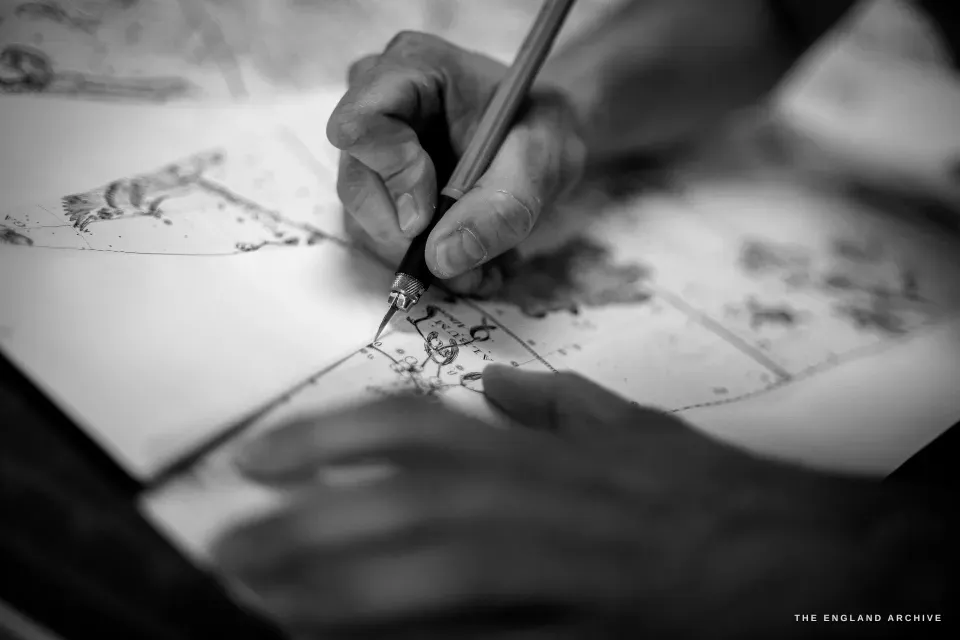 A close view of two hands using a scalpel to cut along the printed line of a celestial chart, constellation figures and stars inked on the sheet.