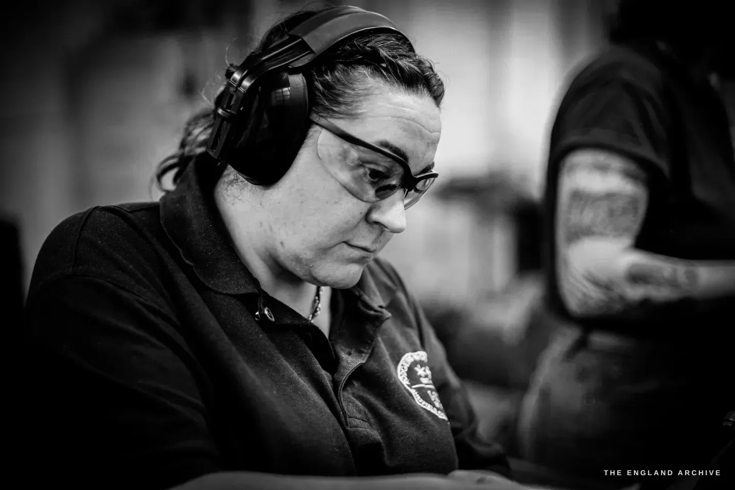 Kylie Cocker concentrates over her work in ear defenders and safety glasses, a colleague&rsquo;s tattooed arm just visible behind her.