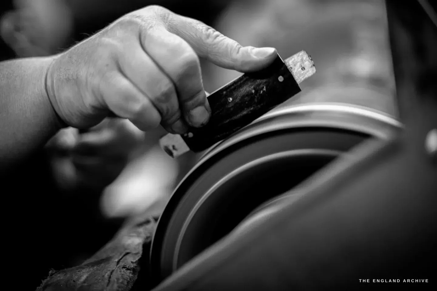 A hand holds a part-finished pocket knife with dark scales against the edge of a spinning grinding wheel.