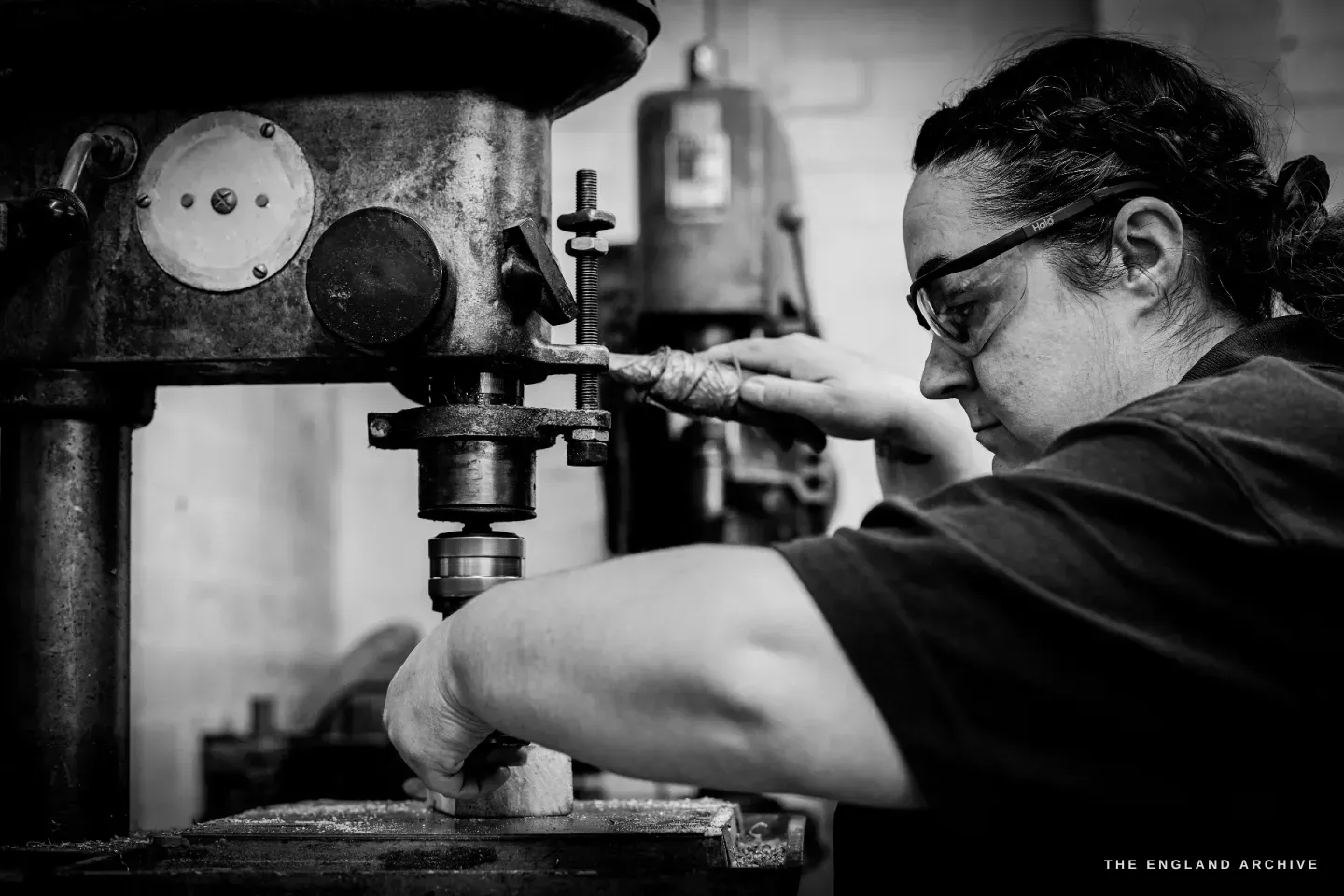 In profile, Kylie Cocker steadies a small part under the descending bit of the pillar drill.