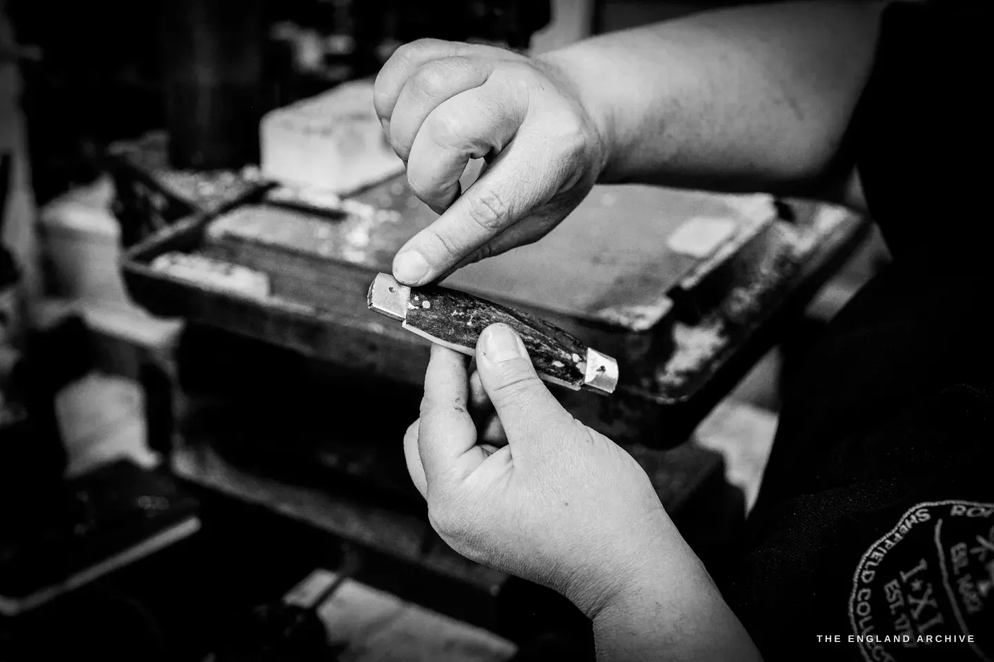 Two hands hold a part-assembled bone-handled pocket knife, checking the fit of the blade against the spring.