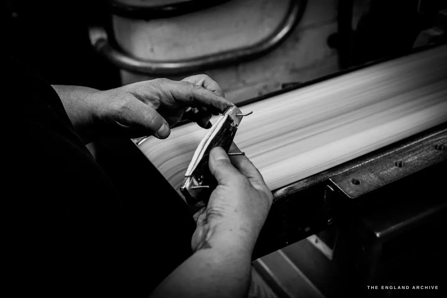 Hands hold a bone-handled pocket knife flat against a long steel finishing surface on the bench.