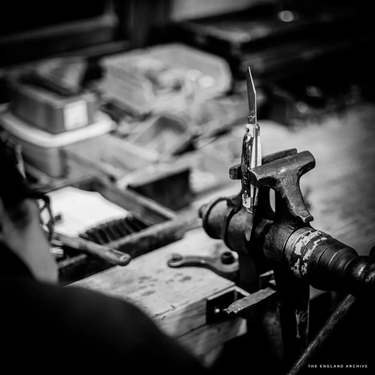 A small pocket knife with its blade open, held upright in a steel stake clamped to the bench.