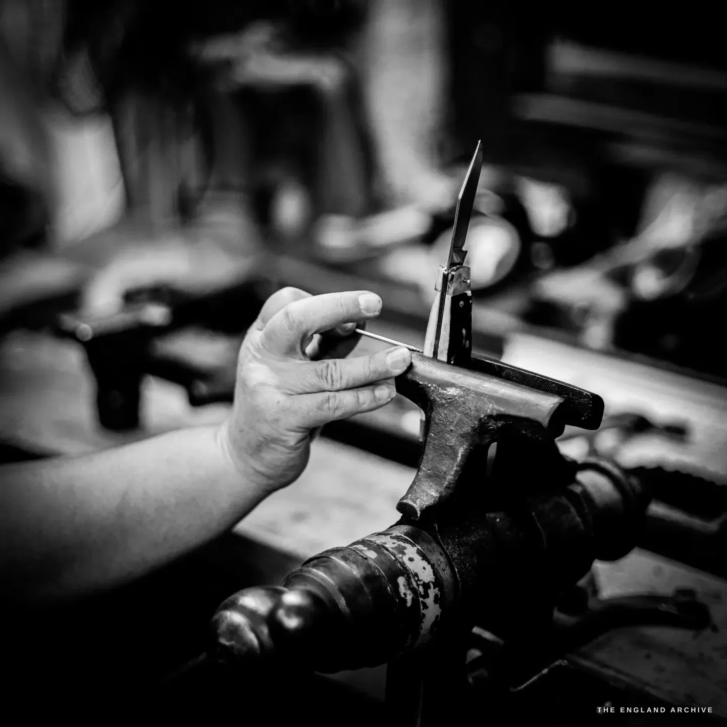 A hand steadies the small steel stake that holds an open pocket knife ready for riveting.