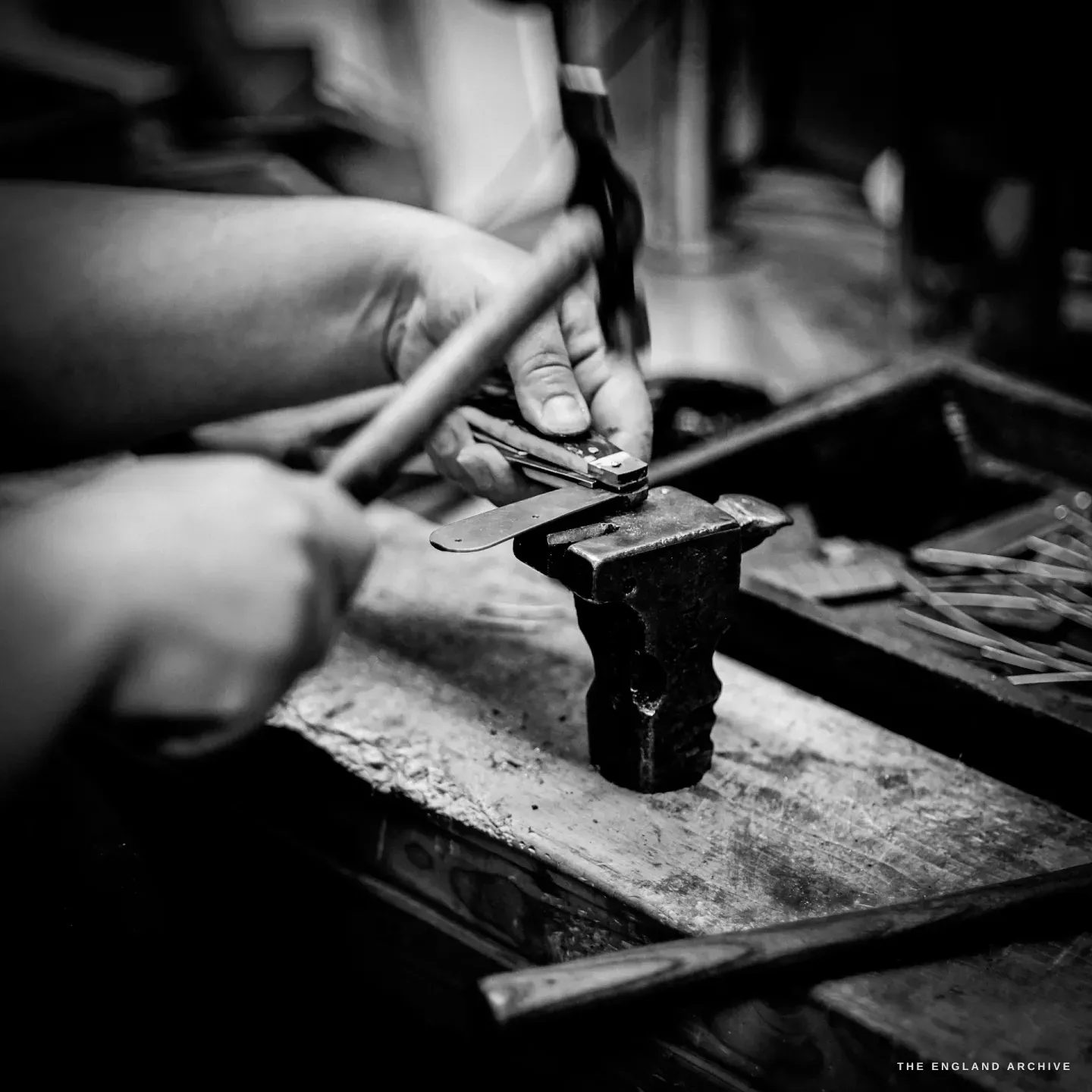 Both hands at work: one holds a fine pin against the knife on the stake, the other taps it with a small hammer.