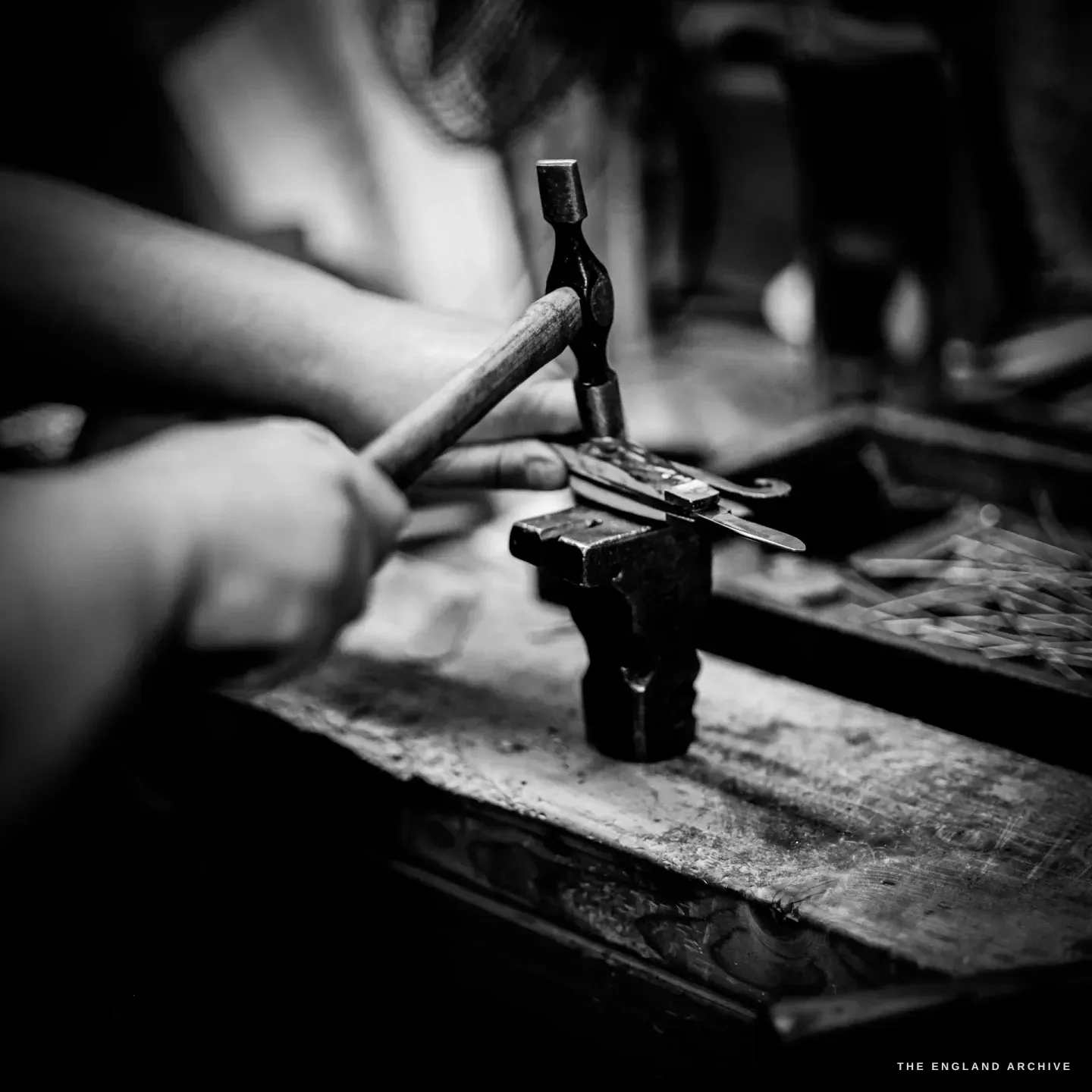 A small ball-pein hammer comes down on the pivot pin of a knife held in the steel stake.