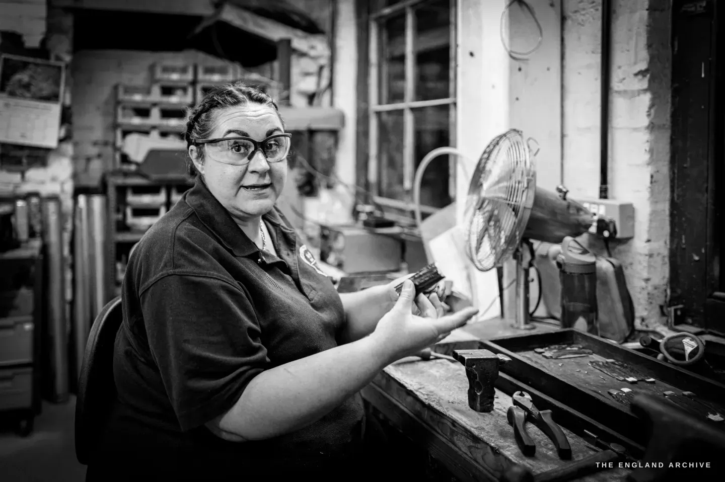 Kylie Cocker turns from her bench to the camera, holding a small part between her fingers, the fan beside her.
