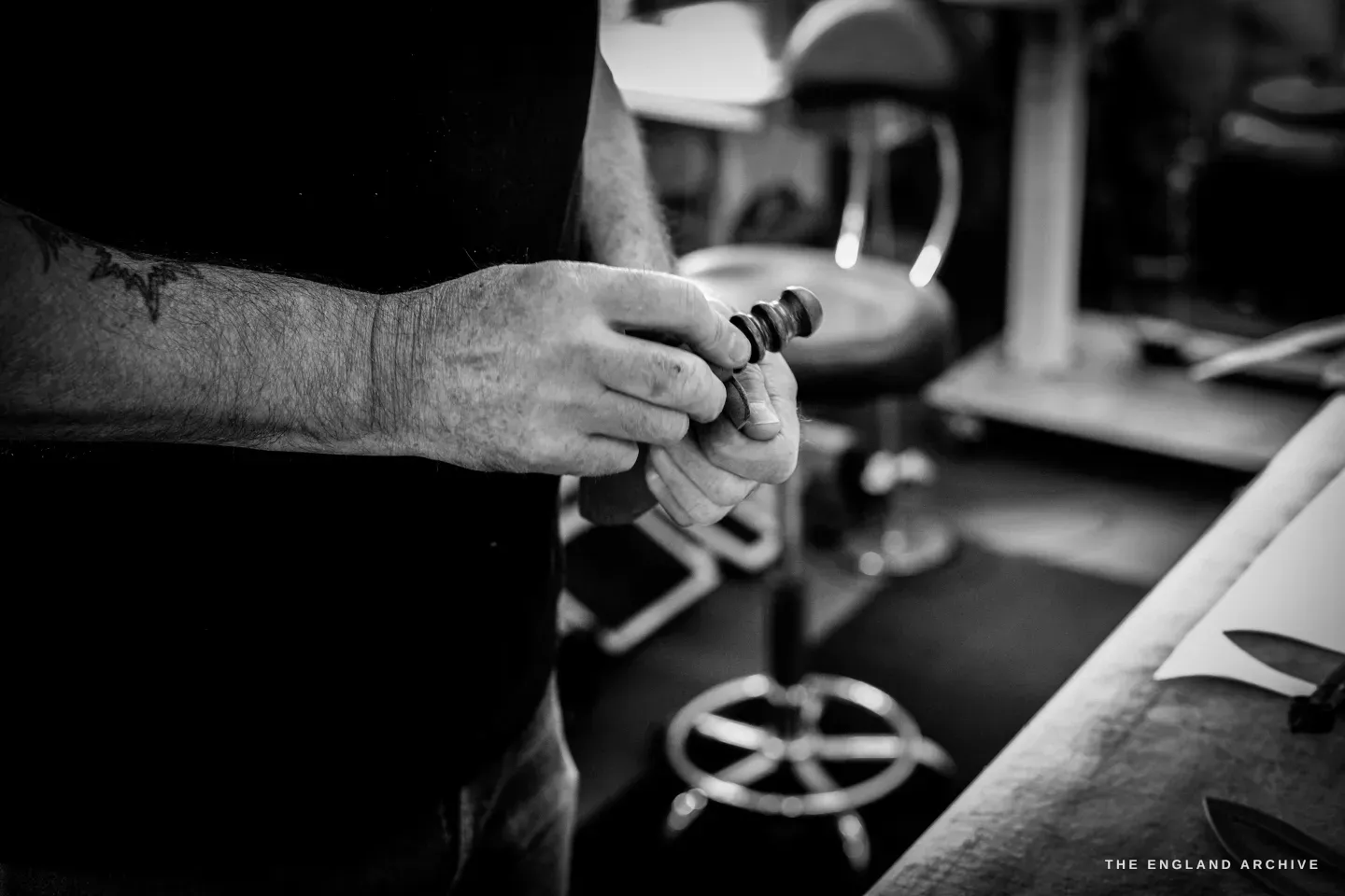 Kevin Wilebore&rsquo;s tattooed hands hold small dark metal buckle parts over the bench.
