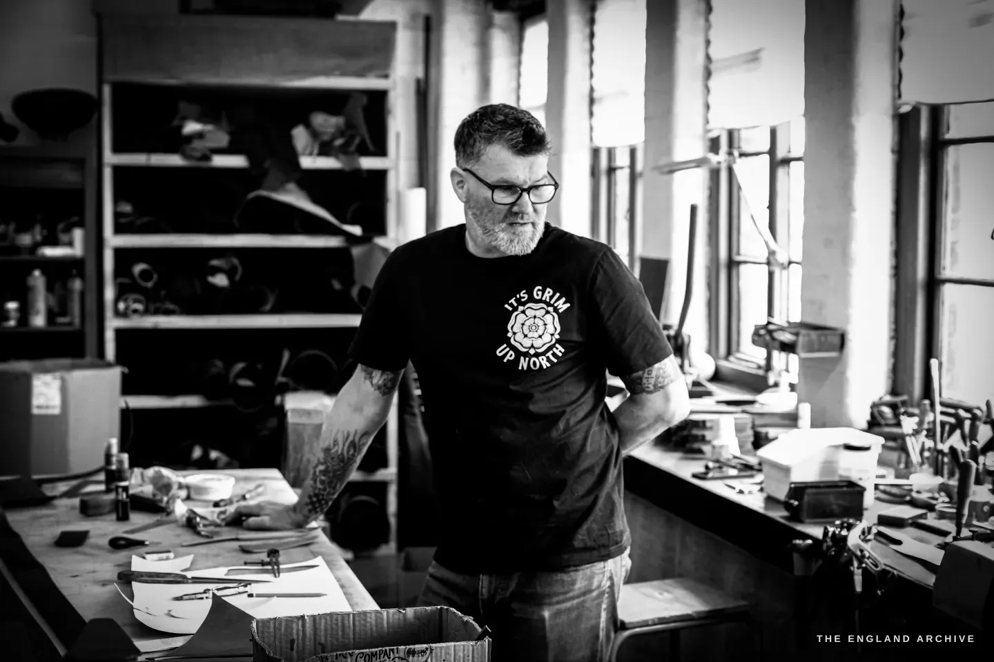 Kevin Wilebore stands at his bench looking down at his work, the bright bench-lined workshop around him.