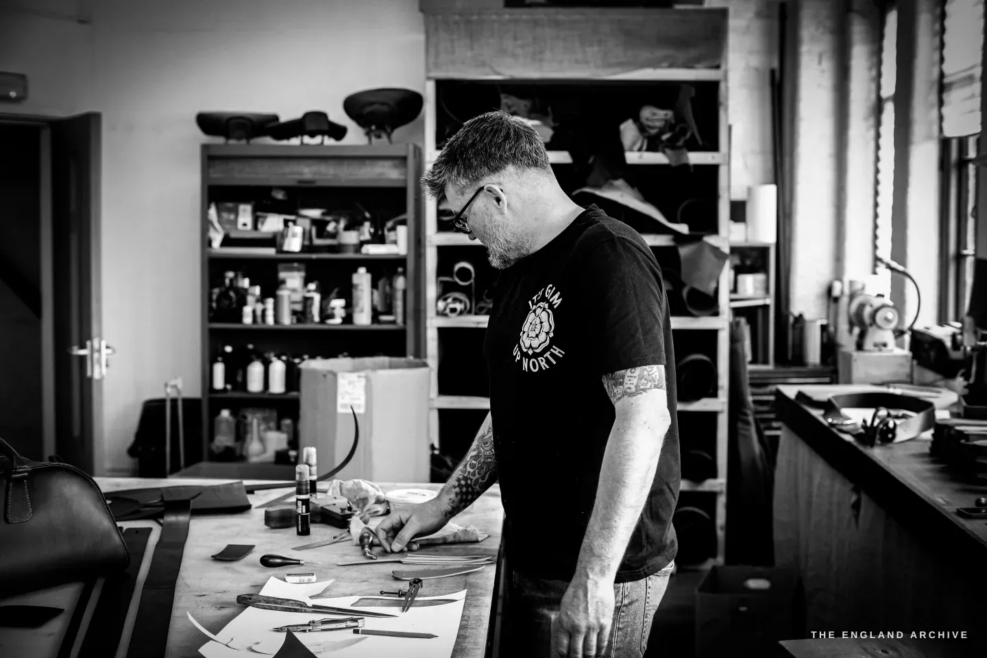 Kevin Wilebore works in profile at the bench, the long workshop and a doorway behind.