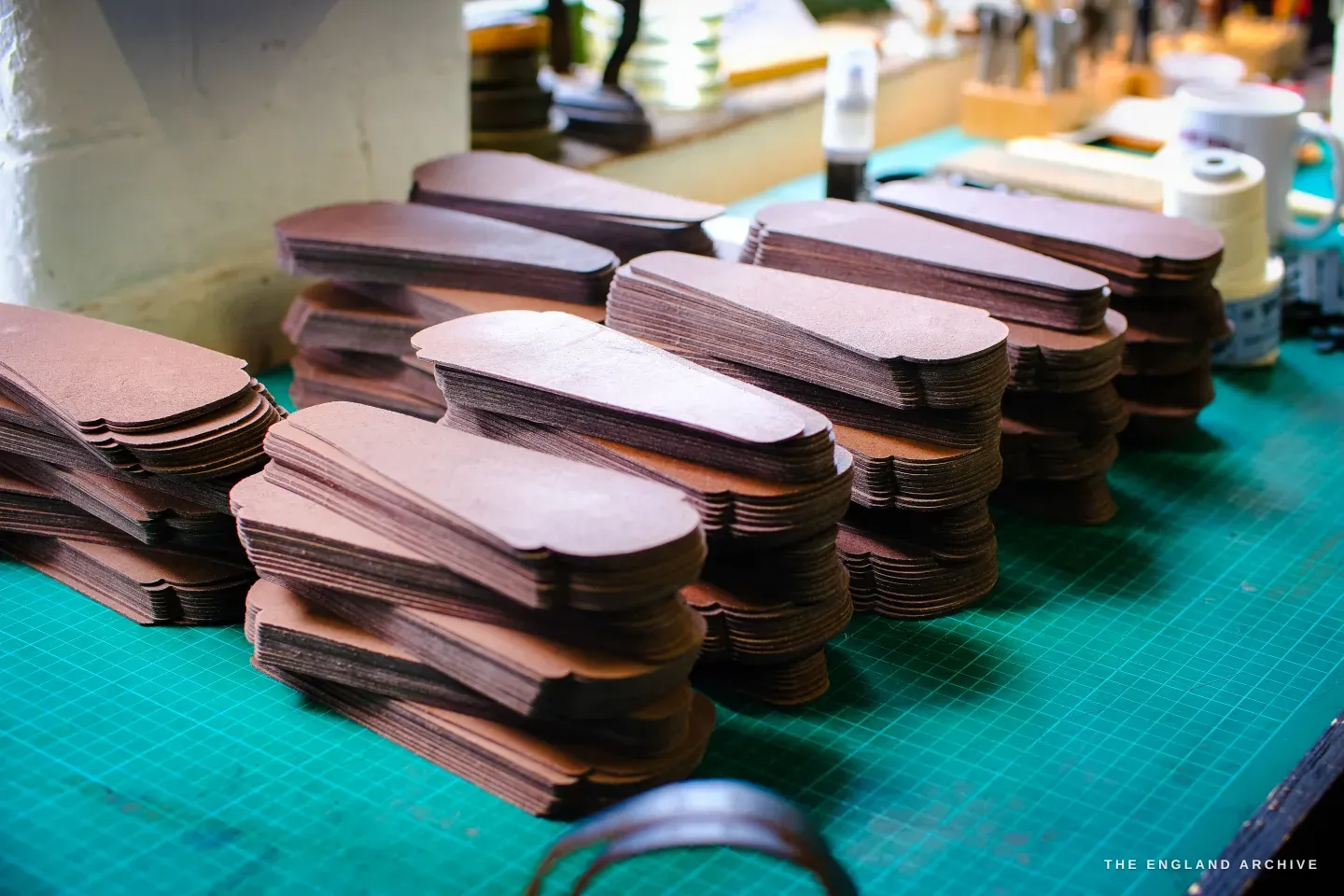 Stacks of cut tan-leather blanks in their finished pouch shape, piled on a green cutting mat.