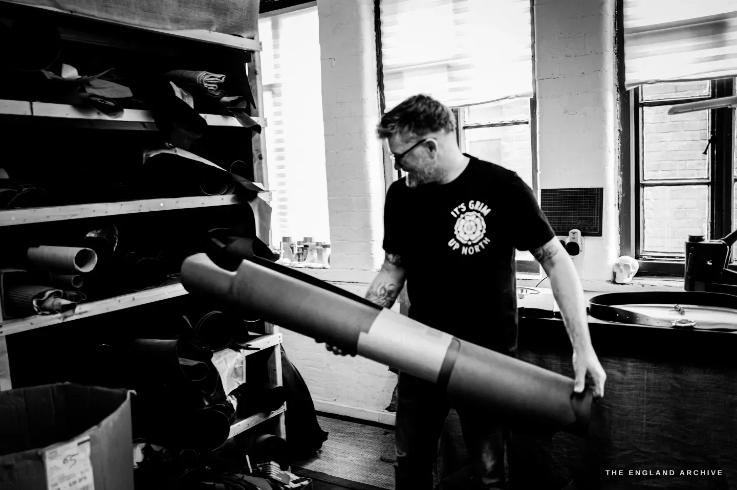 Kevin Wilebore lifts a large roll of material from the storage shelves, the round tanning pans behind.