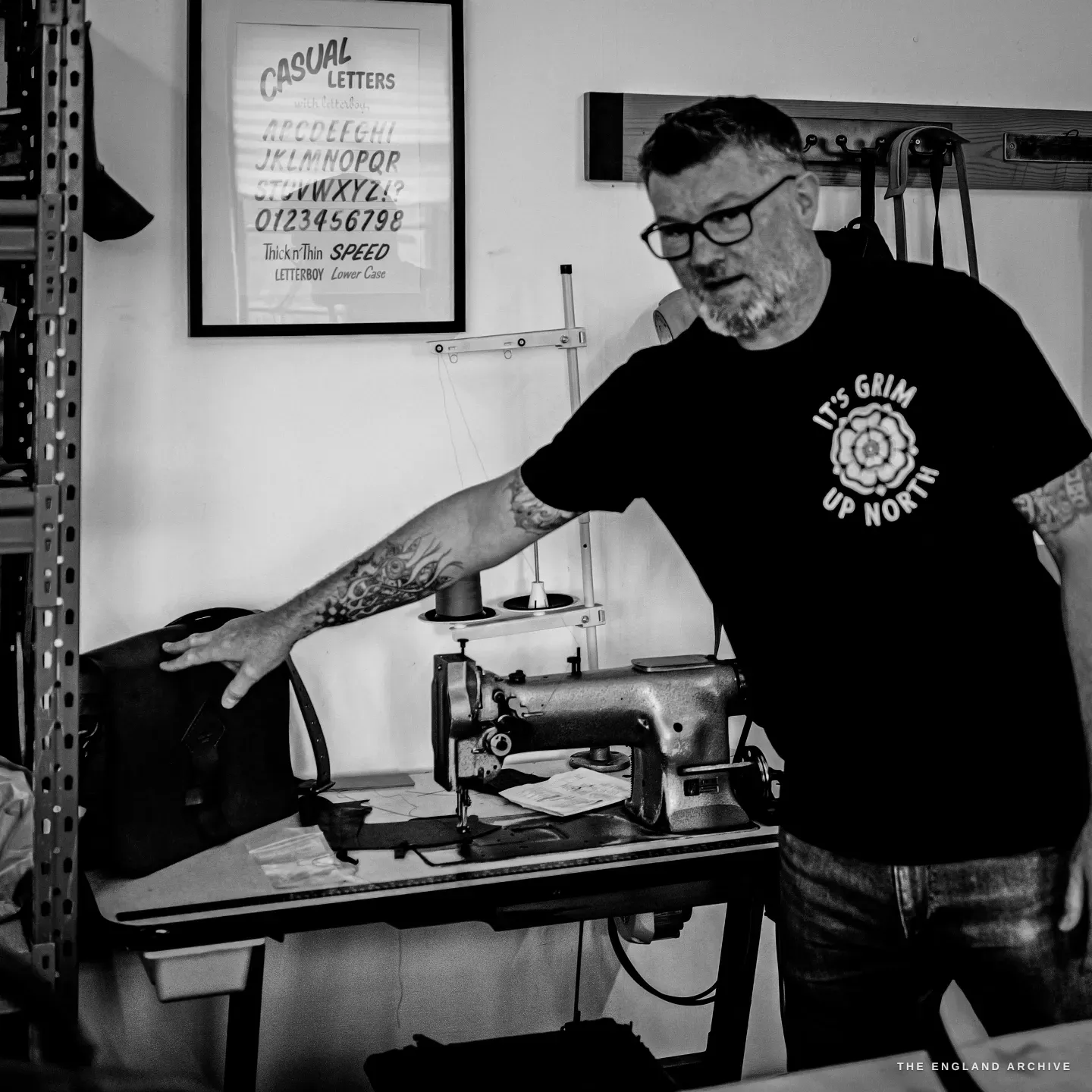 Kevin Wilebore gestures to his vintage industrial sewing machine, a Casual Letters poster on the wall.