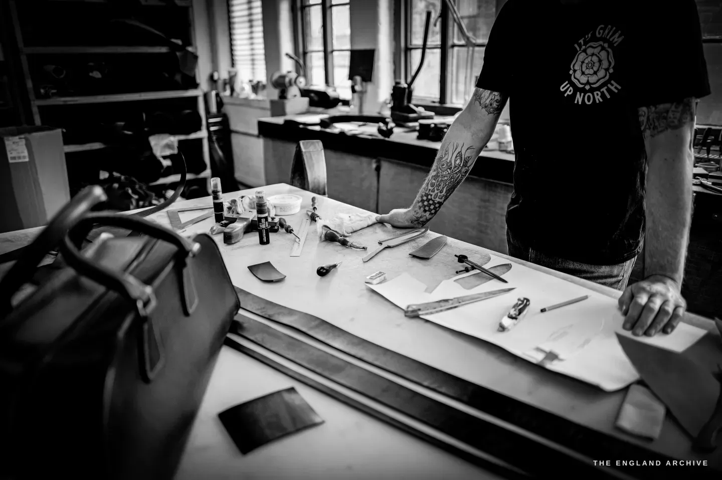 A long workbench laid with leatherworking tools - mallets, pricking irons, knives and edge tools - on a green mat.