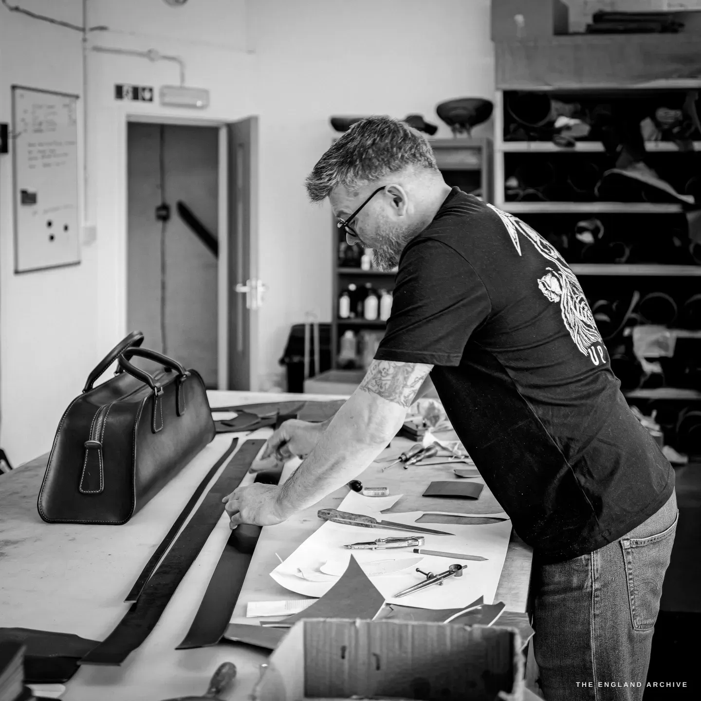 Kevin Wilebore cuts a long strip of leather at the bench, the finished weekender bag beside him.
