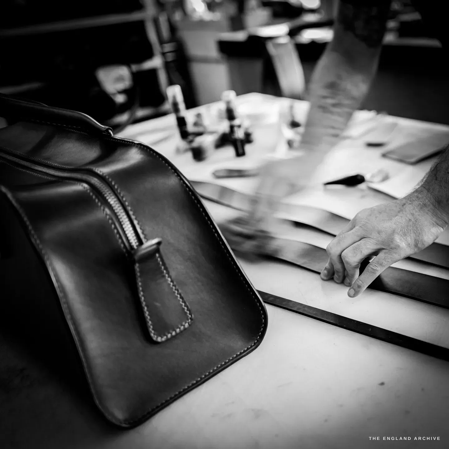 The weekender bag in the foreground as Kevin Wilebore reaches to a stack of cut leather pieces behind.
