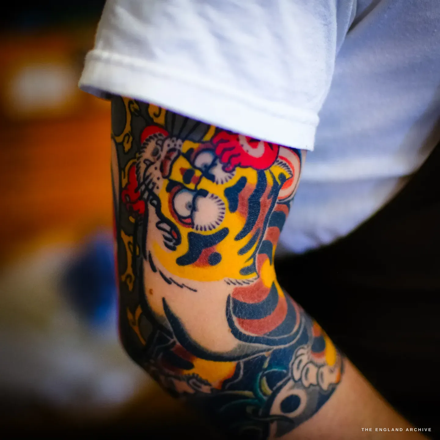 A close view of Léo Lambert's forearm, tattooed in a colourful Japanese style with a dragon in red, orange and gold, below the rolled sleeve of his white t-shirt.
