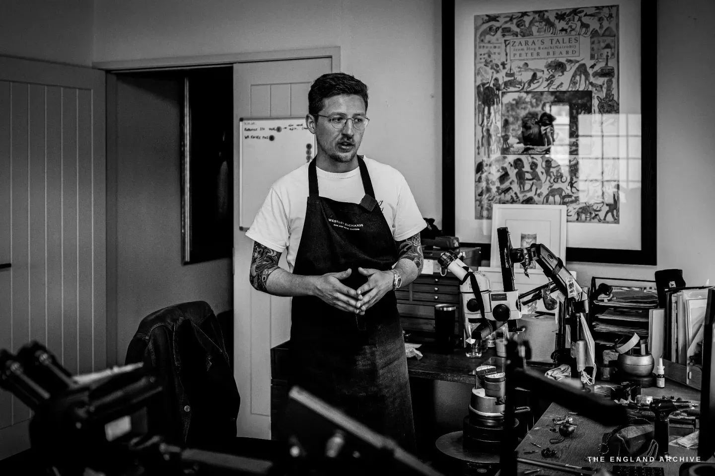 Léo Lambert stands talking in the middle of the studio, a whiteboard and framed prints behind him, microscopes on the bench.