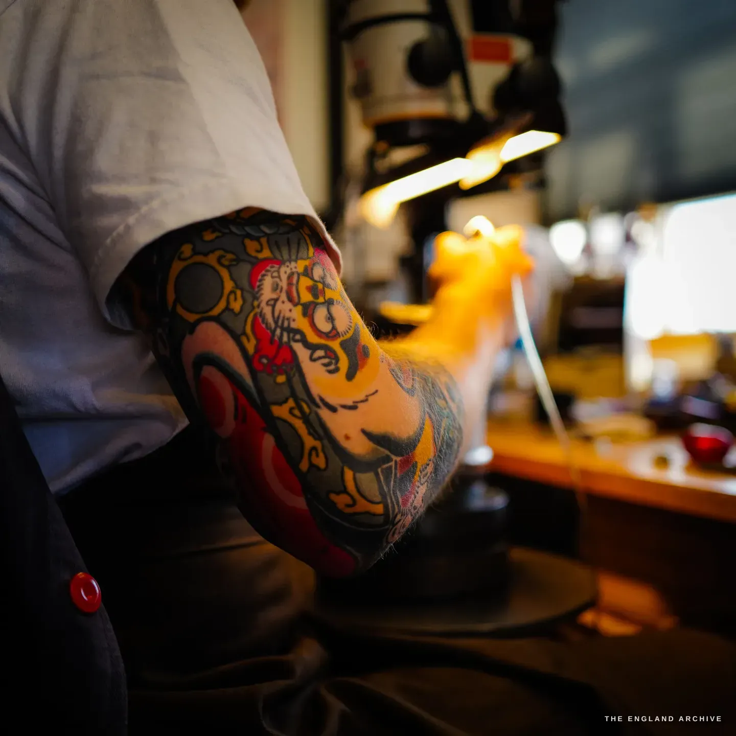 Léo Lambert's colourful Japanese-tattooed forearm as he reaches across the warm-lit bench to his work.