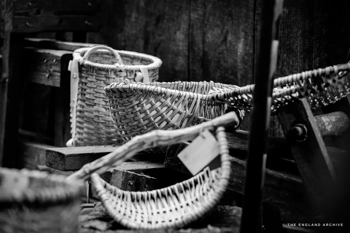 Two finished Whiskets and a smaller Swallow basket lined up along the working bench, a label dangling from one, the older bark surfaces darker than the freshly woven ones.