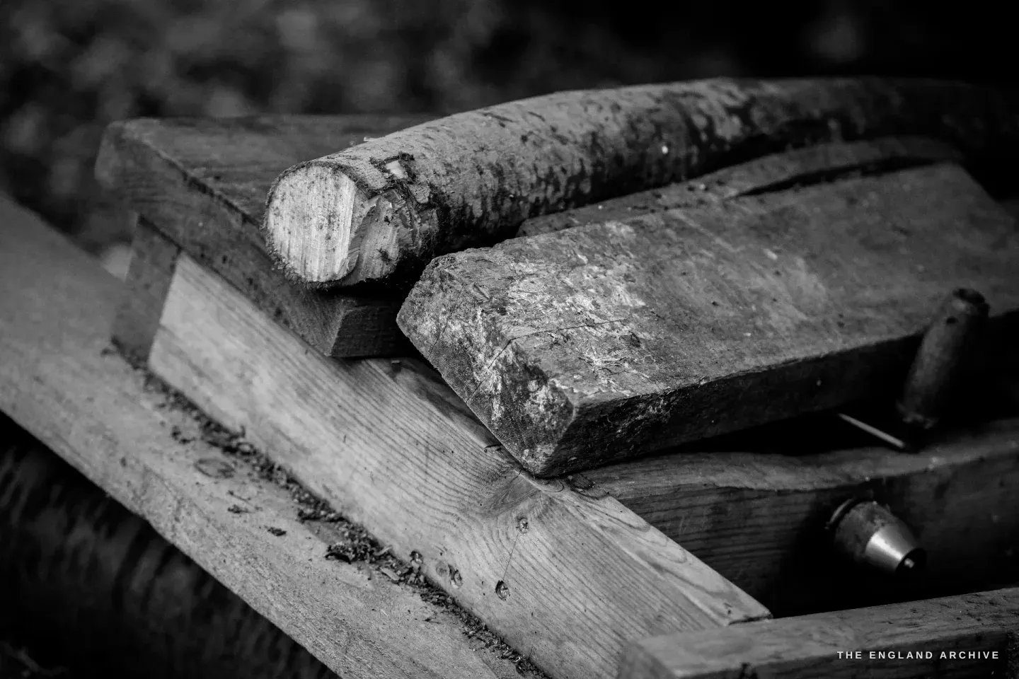 A heavy wooden froe and a wooden mallet resting together on the workbench, the working face of the mallet pitted from years of cleaving.