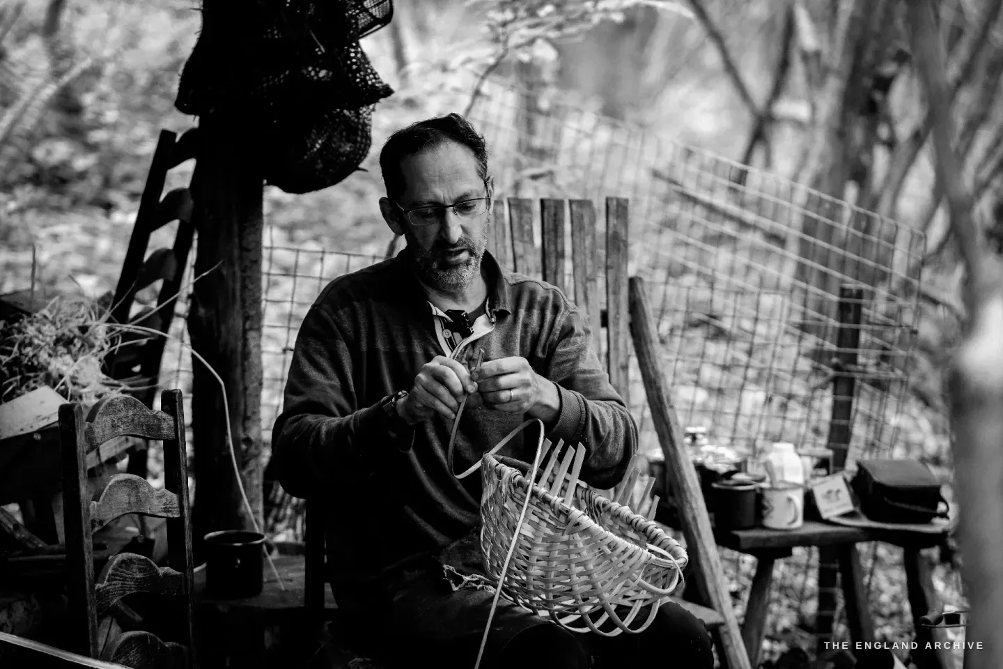 Lewis seated focused on his work, a small splint between his hands, the basket-in-progress balanced on his lap.