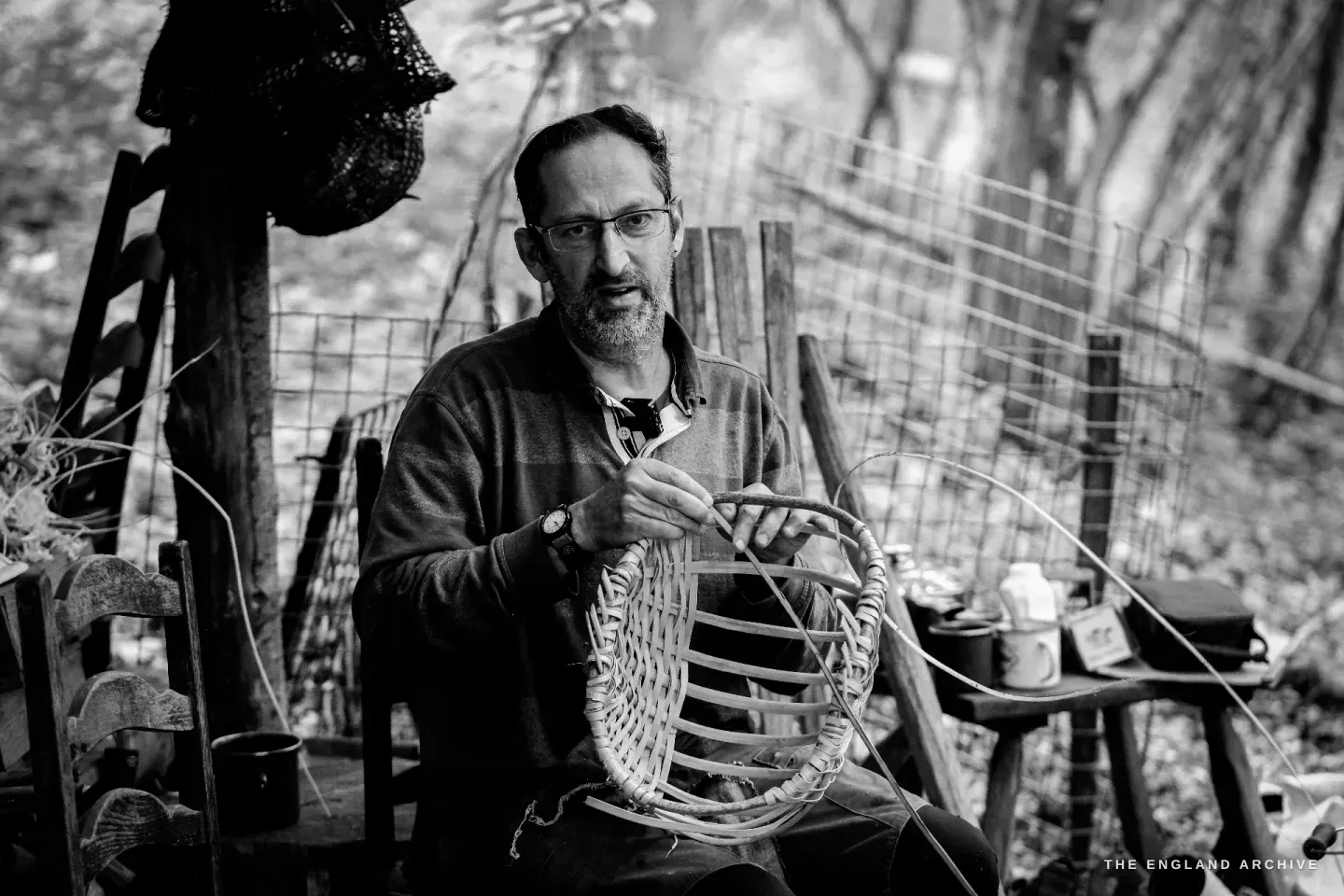 Lewis holds the partial basket frame up between his hands, the radiating splints catching the light from the canopy above.