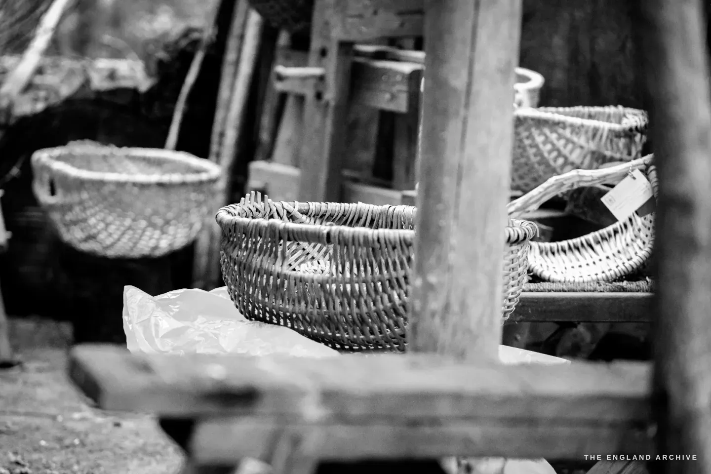A cluster of finished Whisket baskets stacked and leaning on the working bench, each at a slightly different age, some pale and recent, some weathered to a darker tone.