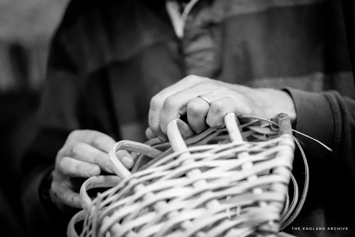 Hands gripping the basket frame from above mid-weave, the radiating splints visible beneath.