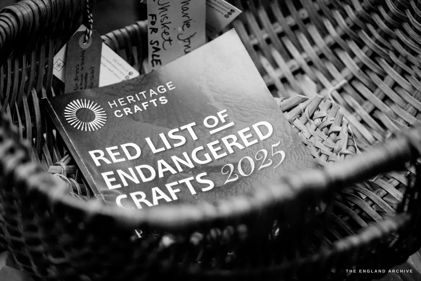 A copy of the Heritage Crafts Red List of Endangered Crafts 2025 booklet sitting inside the Charlie Jones Whisket, surrounded by the basket’s weave.