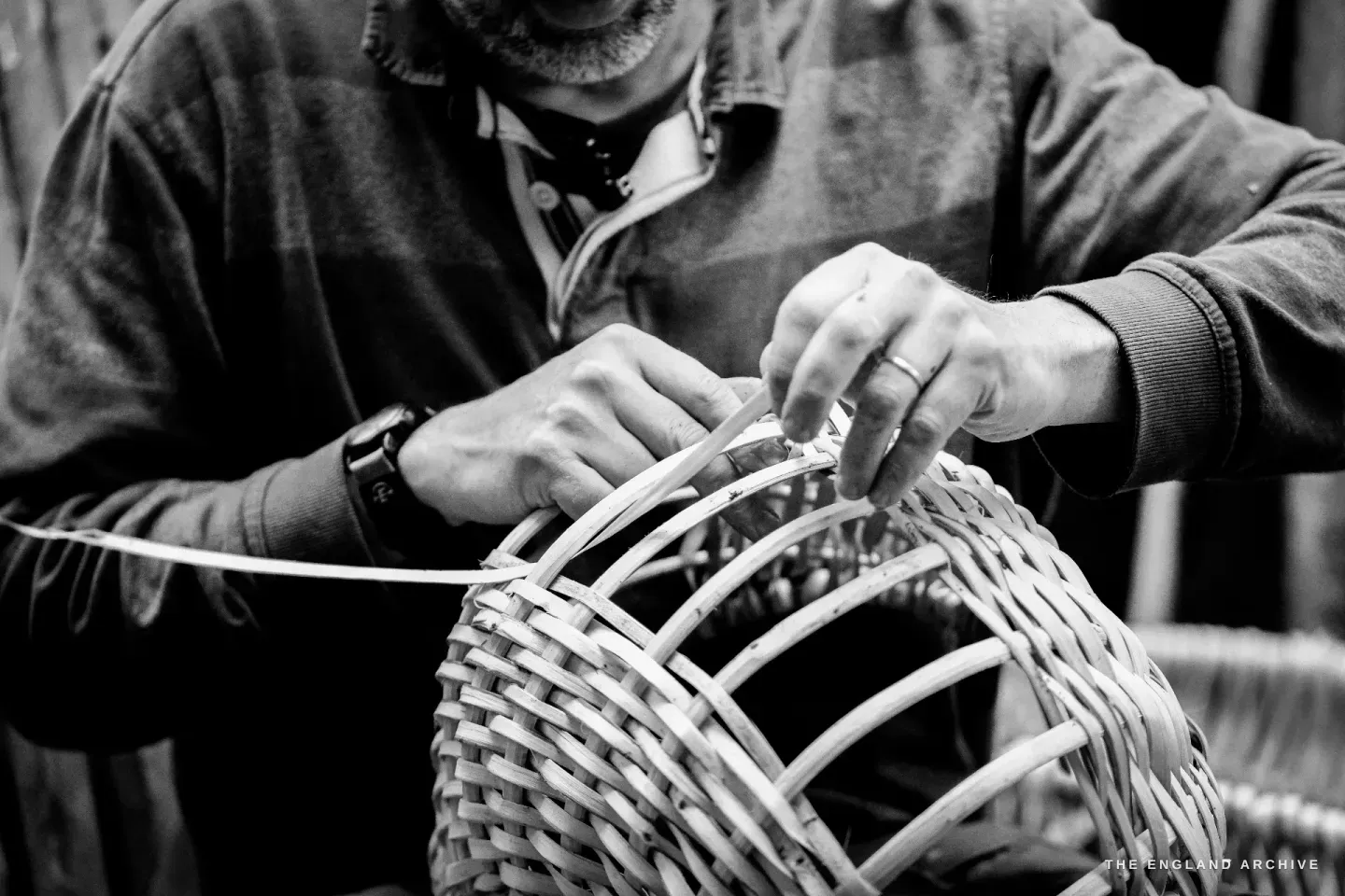 Tight close view of both hands at work on the rim of the basket, fingers tucking a splint into a gap between the standing rods.