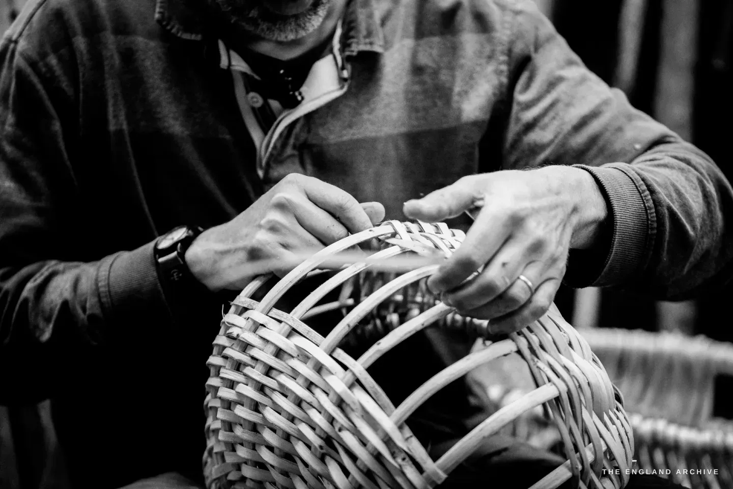 Close view of Lewis’s hands flattening a splint into the weave near the rim, the basket arching up at one side.
