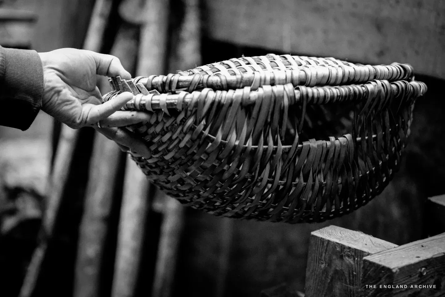 A hand holding the Charlie Jones Whisket out by its handle, the side view of the basket showing the deep round belly and the elegant curve.