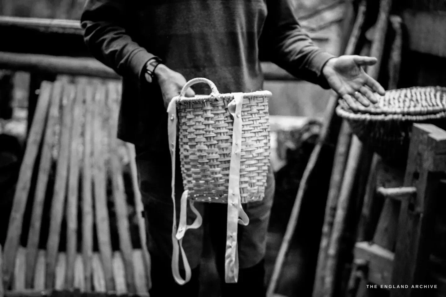 Lewis holding a smaller Swallow basket in front of his body, a leather strap looped through the handle, a larger Whisket visible behind him on the bench.