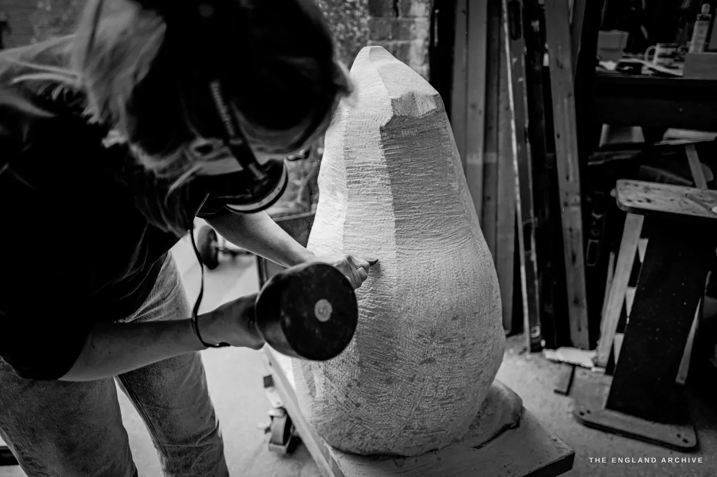 Looking down over Lily Marsh’s shoulder at the head of the sculpture - the chisel biting into a band of rough tooled texture, a smooth dressed facet alongside it, the contrast between worked and unworked stone clear in the raking light.